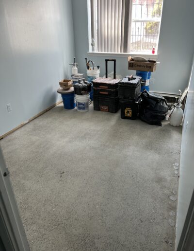 image shows a carpeted room with several cleaning supplies and equipment, including a wet/dry vacuum, some containers, and a cleaning solution